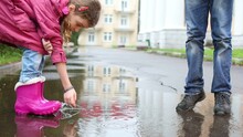 Boy And Girl Play With Paper Boats In Puddle At Cloudy Day 