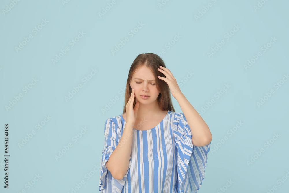 Young woman suffering from toothache on blue background
