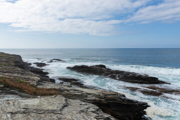 Waves crash on a rocky coast under a partly cloudy sky, capturing nature s serene and rugged beauty