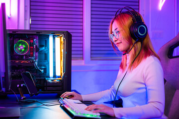 Wall Mural - Young player woman wearing gaming headphones intend to do playing live stream games online at home, Happy Gamer endeavor plays online video games tournament with computer desktop with neon lights