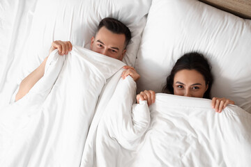 Poster - Young couple lying under blanket in bedroom, top view