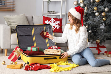 Canvas Print - Woman in Santa hat packing suitcase near Christmas tree