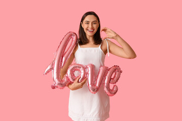 Happy young woman with air balloon in shape of word LOVE on pink background. Valentine's Day celebration