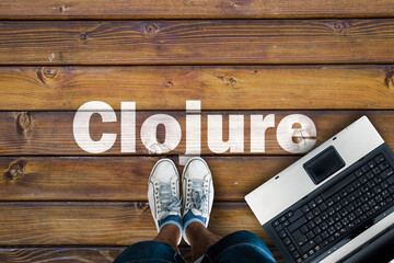 Wall Mural - legs in sneakers standing next to laptop and clojure on wooden floor. clojure programming language.