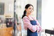 © David - Portrait of happy waitress standing at restaurant entrance. SME entrepreneur young business asian woman attend new customers near door. Smiling small business owner showing open sign in her shop.
