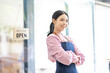 © David - Portrait of happy waitress standing at restaurant entrance. SME entrepreneur young business asian woman attend new customers near door. Smiling small business owner showing open sign in her shop.