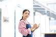 © David - Portrait of happy waitress standing at restaurant entrance. SME entrepreneur young business asian woman attend new customers near door. Smiling small business owner showing open sign in her shop.