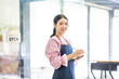 © David - Portrait of happy waitress standing at restaurant entrance. SME entrepreneur young business asian woman attend new customers near door. Smiling small business owner showing open sign in her shop.