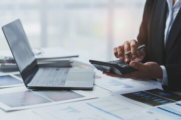 Wall Mural - Asian businesswoman works on laptop and calculates with financial calculator from graphs, statistics, charts. Planning. Business success results in modern office.