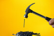 The hammer is hitting the nail, with the nails piled on a yellow background.