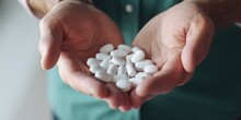 A person holding a handful of pills. This image can be used to illustrate medication, healthcare, or addiction topics