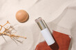 A dry branch, a wooden ball, an unlabeled cosmetic bottle and a notebook stand out against the smooth sand background. Concept of natural cosmetics for skin.