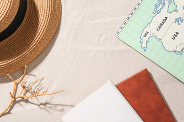 a straw hat, a dry branch, two notebooks and a world map are displayed on the white sand background.