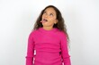 Funny Beautiful teen girl wearing pink sweater over white background makes grimace and crosses eyes plays fool has fun alone sticks out tongue.