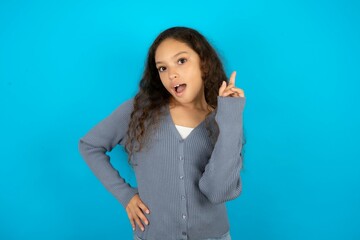 Beautiful teen gil wearing casaul clothes over blue background holding finger up having idea and posing