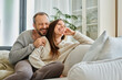 © LIGHTFIELD STUDIOS - laughing man with closed eyes embracing wife on comfortable couch in living room, child-free couple