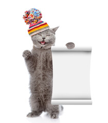 Poster - Happy cat wearing knitted warm woolen hat with pompon shows blank list. isolated on white background