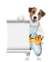 Poster - Funny jack russell terrier puppy wearing denim overalls with tool belt shows empty list. Isolated on white background