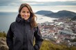© Markus Schröder - Portrait of a blissful woman in her 40s wearing a windproof softshell against a picturesque seaside village. AI Generation