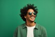 © Markus Schröder - Portrait of a smiling indian man in his 20s wearing a trendy sunglasses against a soft green background. AI Generation