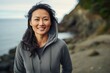 © Markus Schröder - Portrait of a smiling asian woman in her 40s wearing a zip-up fleece hoodie against a rocky shoreline background. AI Generation