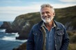 Portrait of a joyful man in his 60s sporting a rugged denim jacket against a rocky shoreline background. AI Generation