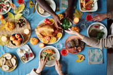 People Sharing Dinner At Fully Arranger Thanksgiving Table Full Of Festive Dishes