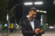 © ADDICTIVE STOCK - Happy Indian businessman in elegant suit using smartphone on city street