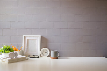 Wall Mural - Home office interior. Picture frame, coffee cup, notebook and pencil holder on white table against brick wall. Copy space.