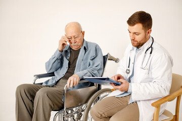 Wall Mural - Male doctor and old man on a wheelchair isolated on a white background