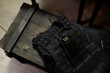 © Seventyfour - Above angle of black protective bulletproof body armor with walkie-talkie in pocket lying on wooden chest in military office