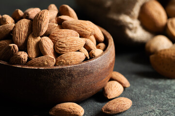 Wall Mural - Delicious sweet almonds in wooden bowl or burlap sack on rustic background, roasted almond nut, healthy food