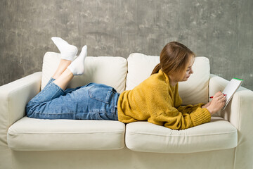 young woman lying on the couch draws in a sketchbook, a white sofa with a gray background