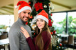 © Minerva Studio - Happy couple in santa hats embracing by the christmas tree.
