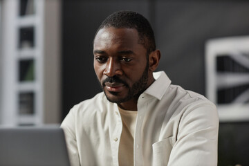 Wall Mural - Portrait of adult African American man looking at laptop screen while working at home office, copy space