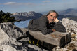 © Guzel - Gray-haired smiling man lying on a wooden bench on the background of a picturesque mountain landscape, Austria