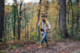 Fototapeta Nowy Jork - In the midst of an autumn hike, a bearded man, a hiker with a backpack and hiking poles, explores the woodland landscape.