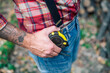 Close-up of lumberjack's hand on a large measuring tape at his waist.