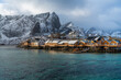 View of a fishermen village with orange wooden houses and green water harbour and snowy mountains