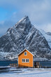 Orange wooden house in Lofoten with snow capped mountain in the background