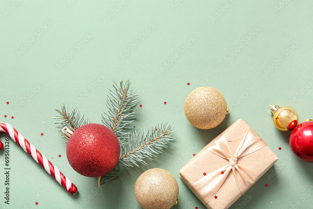 Christmas tree branch with balls, candy cane and gift box on green background
