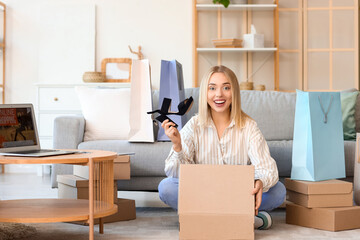 Wall Mural - Young woman with laptop and shopping bags opening boxes of new shoes at home