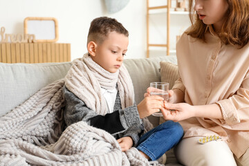 Ill little boy taking pill from his mother at home