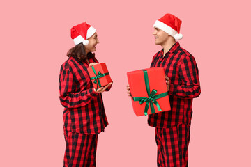 Poster - Happy young couple in Christmas pajamas and with gifts on pink background