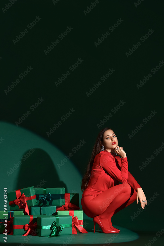 Beautiful young woman with Christmas gift boxes sitting on green background