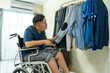 © Kawee - Asian young man sit on wheelchair and choosing clothes on closet rack.