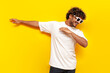young indian guy in sunglasses dancing dab on yellow isolated background, south asian man in white t-shirt