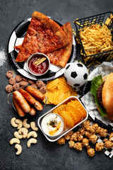 Wall Mural - Saturated fats. Football time. TV remote control and snacks - chips, popcorn, cookies, cheese, sauce, fries, burger, nuts