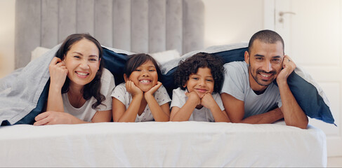 Poster - Portrait, smile and children with parents in bed relaxing and bonding together at family home. Happy, fun and young mother and father laying and resting with kids in bedroom of modern house.