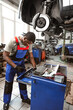 © fotofabrika - African male auto-mechanic repairing car brakes under the car in auto service